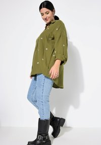 Olijfgroene, knoopsluitingshirt met zilveren sterborduring, gecombineerd met lichtblauwe skinny jeans en zwarte enkellaarsjes met een gespdetail.