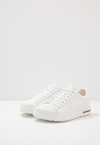 Baskets blanches en cuir avec une finition lisse, bout rond, lacets plats et une semelle intermédiaire texturée comportant une bande d'accent discrète.