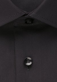 Schwarzer Hemdkragen und Knopfleiste mit zwei schwarzen Knöpfen, einer in Kragenhöhe befestigt und einer darunter.