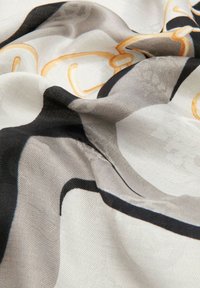 Foulard en soie avec un motif tourbillonnant dans des tons de crème, noir et or, doté d'une texture lisse et d'un éclat subtil.