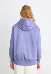 Hoodie lilás claro com um capuz espaçoso, punhos e bainha canelados. Feito de material suave, apresenta um design simples e elegante.