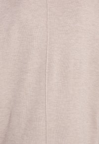 Tessuto a maglia beige chiaro con una texture liscia, caratterizzato da una cucitura centrale che corre verticalmente lungo il centro.