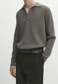 Brun, ribbet langærmet polo-shirt med krave, parret med mørkegrønne bukser og et sort bælte. Enkelt, tekstureret design.