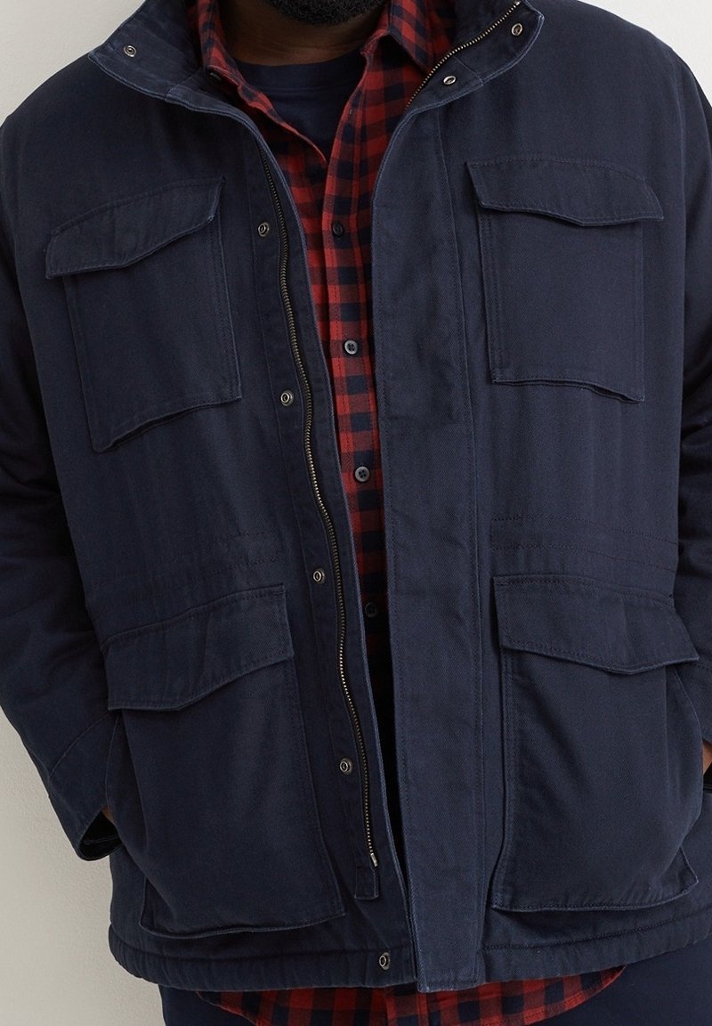 Homme portant une veste bleu marine avec quatre poches à rabats sur une chemise à carreaux rouge et noire.