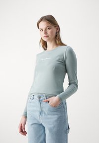 Mėtų žalios spalvos ilgos rankovės marškiniai, pagaminti iš minkštos medvilnės, su baltu "Pepe Jeans London" logotipu, atspaustu ant krūtinės. Kasdienis derinys.