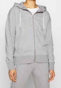 Grijze hoodie met rits van een zachte katoenmix, met een rits aan de voorkant, witte trekkoorden en zijzakken. Logo subtiel weergegeven op de borst.
