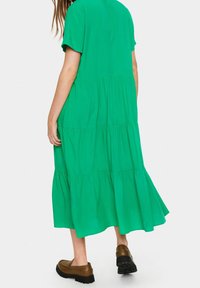 Robe midi verte à étages faite d'un matériau doux, avec des manches courtes et un ourlet évasé, associée à des chaussures marron.