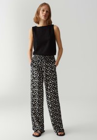 Zwart gebreid mouwloos topje gecombineerd met wijde broek met een zwart-wit abstract patroon. Het model draagt zwarte sandalen.