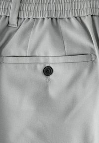 Light gray shorts featuring an elastic waistband with a button closure and a back pocket. Material has a soft, smooth texture.