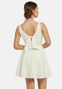Weißes Kleid mit V-Ausschnitt und Schleifenakzent. Skater-Stil, ärmellos mit einem ausgestellt geschnittenen Rock. Glatte Stoffstruktur.