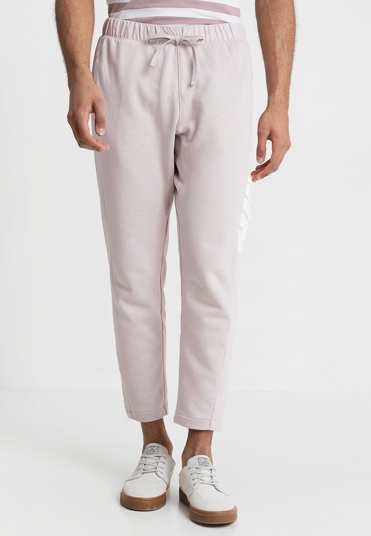 Light pink joggers with an elastic waistband and drawstring; tapered fit with a smooth texture and a subtle logo detail on the side.