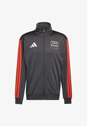 Giacchetto sportivo nero con cerniera completa, strisce rosse sulle maniche, logo Adidas sul petto sinistro e marchio Audi Revolut F1 Team sul petto destro.
