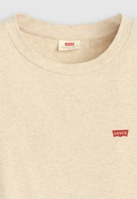 Šviesiai ruda, vertikaliomis juostelėmis megzta marškinėlių suapvalintais kaklais, su tekstūra ir raudona Levi's logotipo etikete kairiajame šone.