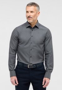 Grijze button-up overhemd met een getextureerd patroon, lange mouwen en zwarte knopen; gecombineerd met donkere broeken en een bijpassende riem.