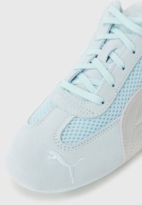 Light blue sports shoe featuring mesh panels and suede accents. Flat laces and a small logo on the side highlight its design details.