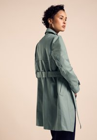 Mintgrön trenchcoat med skräddarsydd passform, midjebälte och detalj med bakslits. Slät tyg och lång ärm. Enkel, funktionell design.