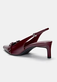 Chaussures slingback en cuir verni bordeaux avec un bout pointu, un talon de 5 cm et des accents de boucles décoratives à l'avant. Fini lisse et brillant.