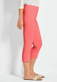 Koraal kleurige capri-broek met zijslits aan de zoom, gemaakt van lichtgewicht stof. Gecombineerd met lichtgekleurde platte sandalen.