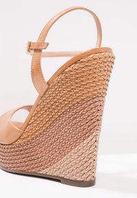 Sandale compensée avec bride de cheville en cuir beige et talon tressé texturé multicolore en tons sable, marron et crème.