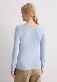 Lichtblauw langemouwen top met een ronde halslijn en een aansluitende silhouet, gemaakt van zachte, gestructureerde stof. Bevat stiksel details langs de achterkant.