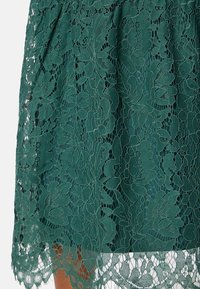 Groene kantrok met ingewikkelde bloemmotieven en textuurgeborduur, met een scalloped zoom en een lichtgewicht stof.