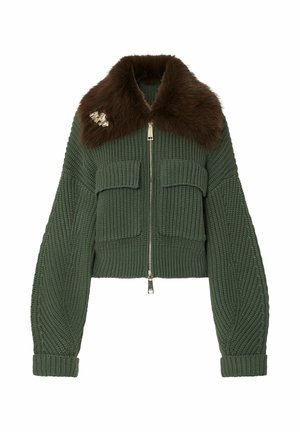 Chaqueta verde de punto con cremallera, gran cuello de piel marrón y dos bolsillos frontales con solapa, con un broche dorado en el cuello.