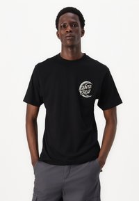 Schwarzes Baumwoll-T-Shirt mit einem runden Grafiklogo und dem Text "SANTA CRUZ" auf der linken Brustseite. Kurze Ärmel und Rundhalsausschnitt.