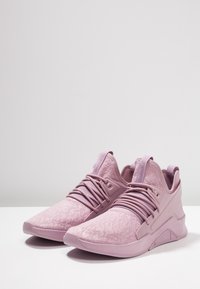 Ljusrosa sportskor med ett texturerat övermaterial, tydligt snörningssystem och en böjd sulkonstruktion. Sval yta och minimal märkning.