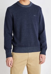Marineblauer Pullover mit strukturiertem Finish, geripptem Halsausschnitt und Bündchen sowie subtilen helleren Sprenkeln. Verfügt über ein Logo auf der Brust und eine klassische Silhouette.