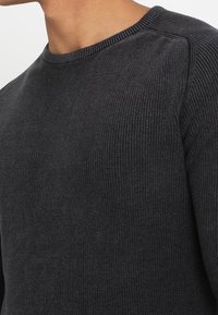 Dunkelgrauer gerippter Pullover mit rundem Ausschnitt und dezentem Strukturmuster, gefertigt aus weichem Strickmaterial für eine figurbetonte Silhouette.