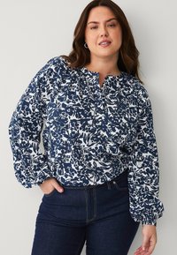Navy en witte bloemetjesblouse met een ronde halslijn, lange pofmouwen en een losse pasvorm, gecombineerd met donkere spijkerbroek.