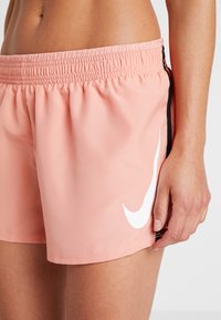 Lichtroze sportshorts met een elastische tailleband, voorzien van een wit Nike-logo aan de zijkant en zwarte accenten. Soepele textuur.