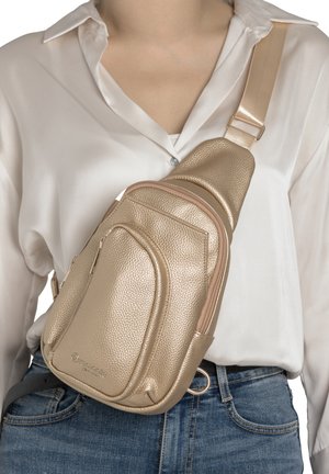 Person trägt eine metallisch goldene, strukturierte Umhängetasche über einem weißen Hemd und blauen Jeans mit schwarzem Gürtel.