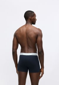 Dark blue, cotton boxer shorts with a white elastic waistband featuring Calvin Klein branding. View from the back. Smooth texture.