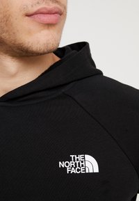 Felpa nera in cotone con cappuccio, caratterizzata da un logo bianco de "The North Face" sul lato sinistro del petto, dotata di cappuccio con cordini e polsini a coste.