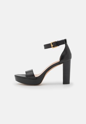 Sandale noire à talons hauts avec une plateforme, tige en cuir lisse, bride de cheville ajustable et détail de boucle en ton doré.