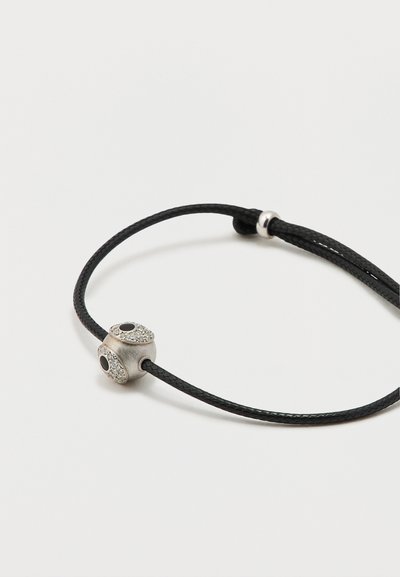 Mustast punutud nöörist käevõru, millel on hõbedane ripats kahe tekstuurse, särava otsaga ja mustade akentsõlmedega. Lihtne, reguleeritav disain.