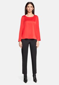 Rød satin langærmet top med rund halsudskæring, kombineret med sorte skræddersyede bukser og sorte spidse ankelstøvler. Glat tekstur og løs pasform.