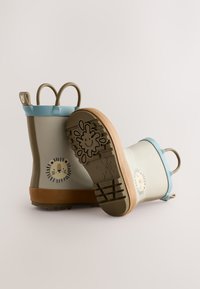 Stivali da pioggia beige per bambini con rifiniture blu, suole marroni, volto di leone sul lato e motivo del sole sorridente sul battistrada.