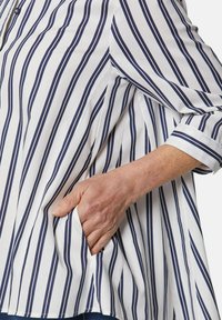 Gestreifte Bluse mit weißen und navy-blauen vertikalen Streifen, leichtem Stoff, einer Tasche auf der linken Seite und hochgerollten Ärmeln.