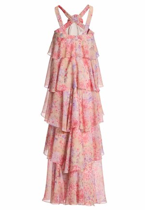 Vrouw draagt een mouwloze, gelaagde roze maxi-jurk met bloemenprint en een grote bloemdetail bij de halslijn, gecombineerd met zilveren open-toe hakken.