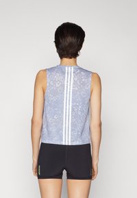 Ærmeløs lavendel tanktop med en tekstureret dyreprint og hvide lodrette striber på ryggen, parret med sorte shorts med grønne detaljer.