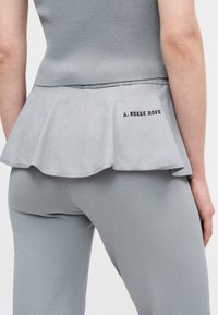 Γκρι τοπ με ριγωτή υφή, φαρδιά βάση και λογότυπο στο πίσω μέρος, σε συνδυασμό με γκρι εφαρμοστά κολάν. Ομαλή υφή συνολικά.