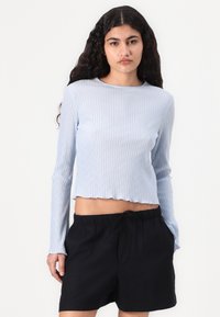 Lichtblauw geribbeld longsleeve top met een cropped zoom, gecombineerd met zwarte shorts met trekkoord. De top heeft een ronde halslijn.