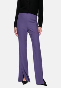 Purple, high-waisted trousers with a straight leg and slight side slits at the hem, paired with a black textured cardigan.