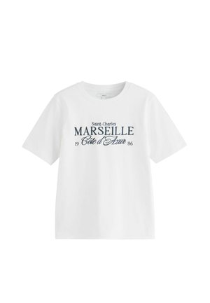 Fehér rövid ujjú póló tengerészkék szöveggel: „Saint-Charles MARSEILLE Côte d'Azur 1986“, elől középen nyomtatva.
