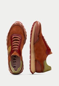 Sneakers in suede marrone con una combinazione di accenti in pelle rossa, sovrapposizioni testurizzate e un tallone verde; presentano lacci a contrasto e una suola in gomma.