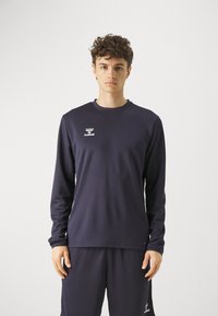 Maglietta atletica a maniche lunghe navy con colletto rotondo, caratterizzata dal logo Hummel in bianco. Il tessuto appare liscio con una vestibilità regolare.