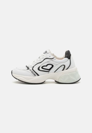 Sneaker in pelle bianca con accenti neri, design a forma di cuore, suola spessa, dettagli testurizzati e logo sul lato. Chiusura con lacci.