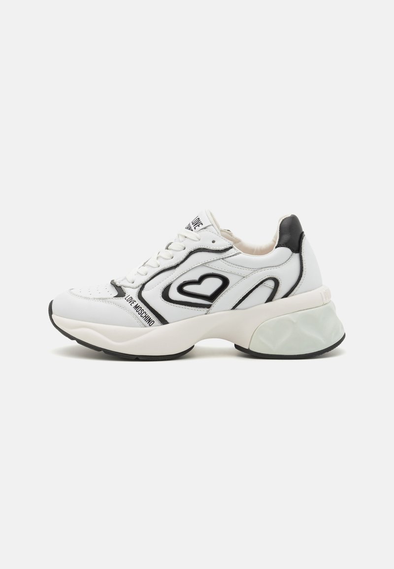 Hvit skinnsneaker med svarte detaljer, hjerte-design, tykk såle, teksturerte detaljer og logo på siden. Snøring.